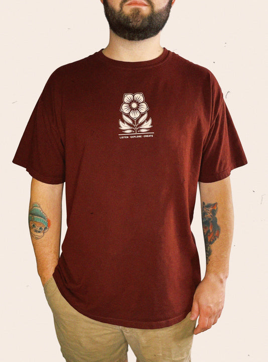 Maroon Comfort Colors tee embellished with a floral logo and the words Listen. Explore. Create.